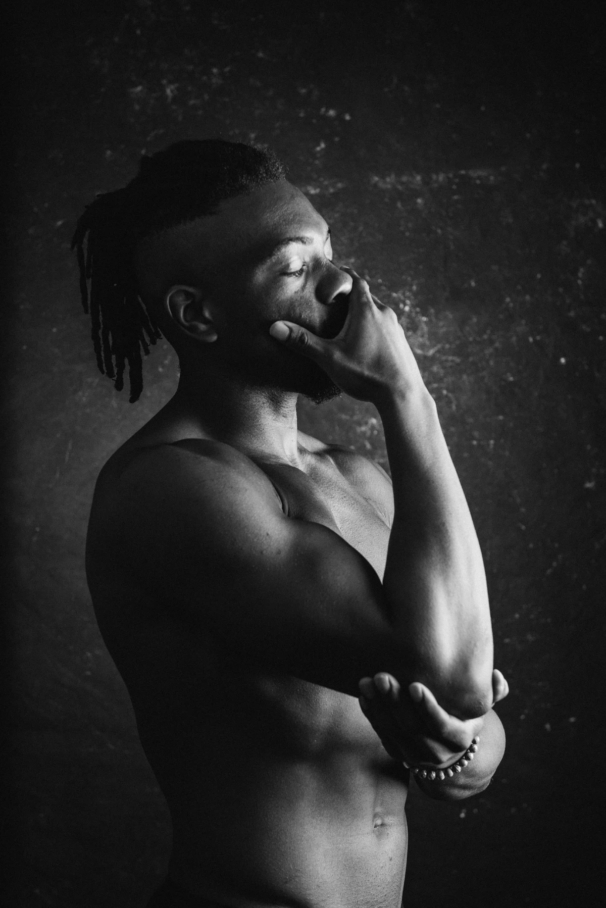 Shirtless person with closed eyes holds their face with one hand and supports their elbow with the other