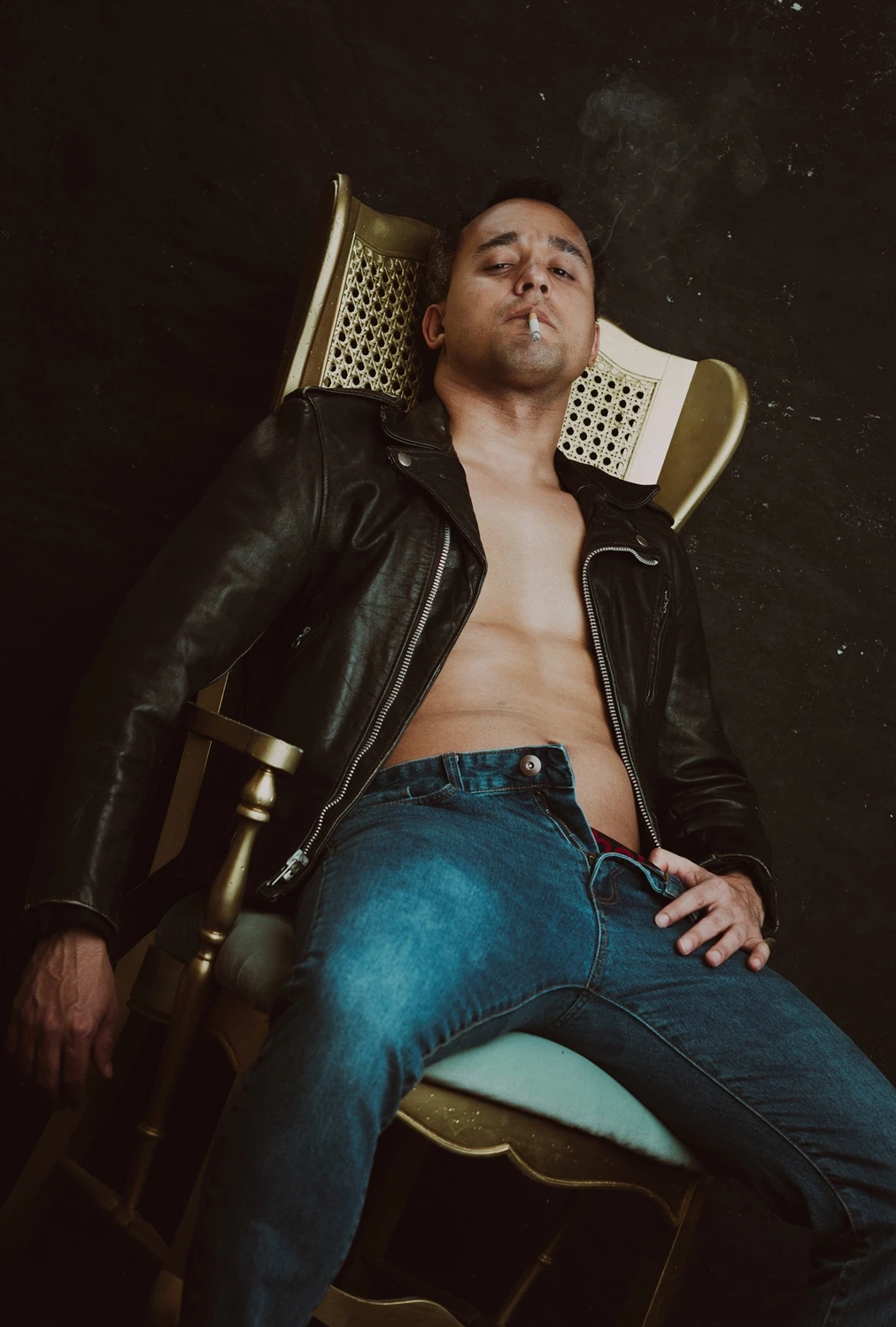 a man sitting on a coach wearing a leather jacket for a men's boudoir session